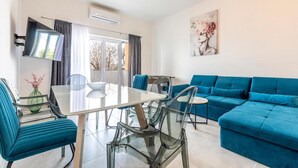 Een moderne woonkamer met een blauwe bank, een glazen eettafel en turquoise stoelen.
