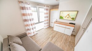 Una sala de estar con un sofá, un televisor montado en la pared y una zona de cocina con armarios y una encimera.