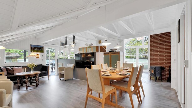 A spacious living area with a dining table, sofas, and a kitchen area with a brick wall and large windows. - Stunning home in Rømø with kitchen (Rømø)
