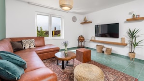 Un salon avec un canapé en cuir, une table basse, un téléviseur et une grande fenêtre.