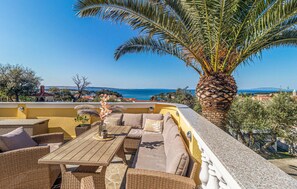 Enjoy breathtaking views of the sea and distant hills from this rooftop terrace, featuring wicker furniture and a beautiful palm tree.