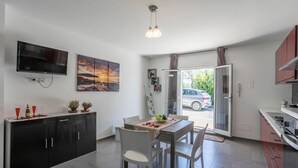 A modern kitchen with a dining area, a TV mounted on the wall, and a view of the street outside.