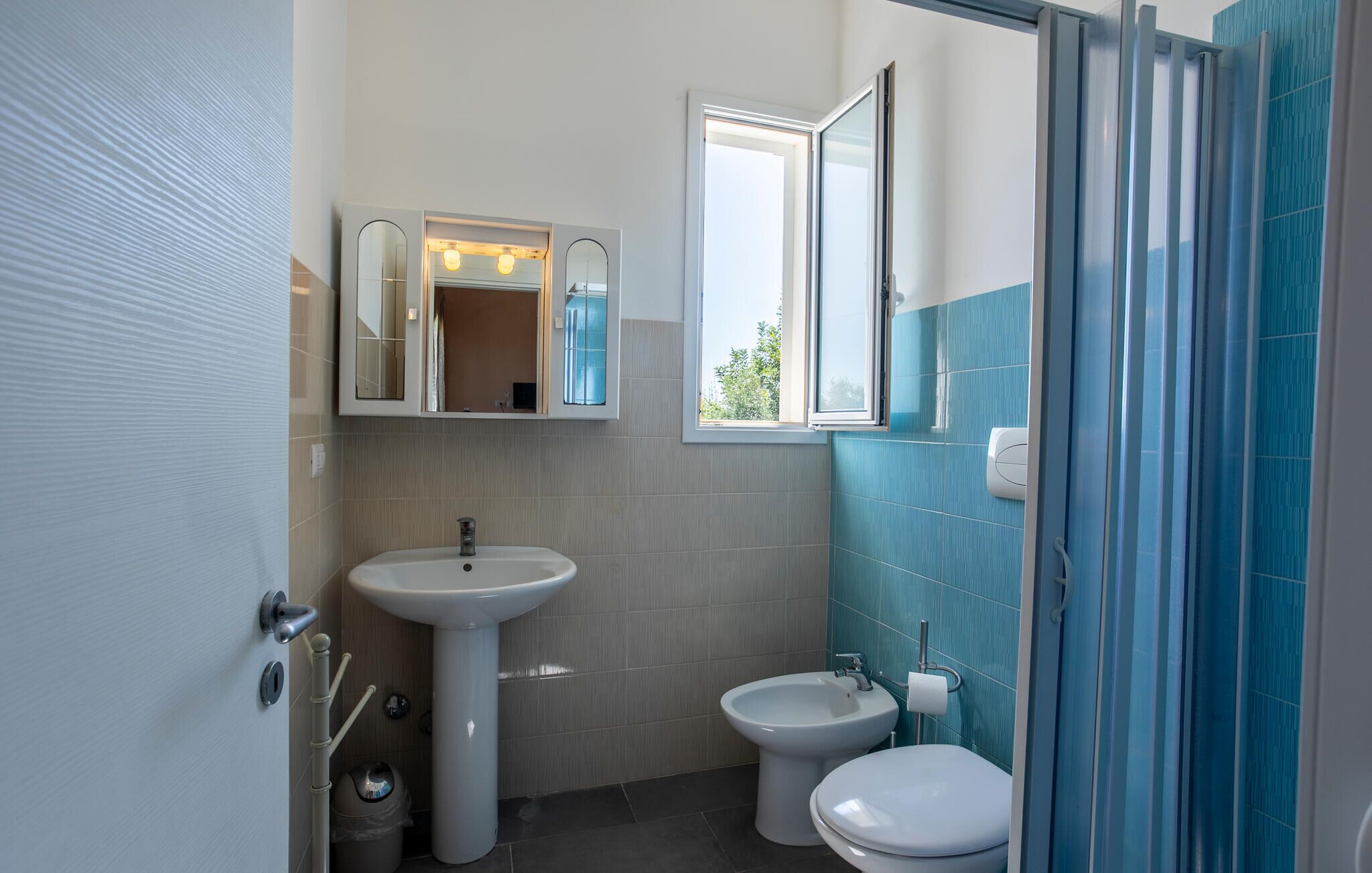 A bathroom with a sink, bidet, toilet, and a window.