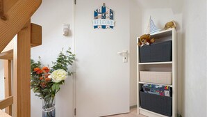 Una puerta blanca con un letrero que dice 'WELCOME', un florero con flores y una estantería con cajas de almacenamiento.