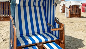 Una silla de playa con cojín azul y blanco a rayas, estructura de madera y toldo blanco con la inscripción 'WANGERLAND'.