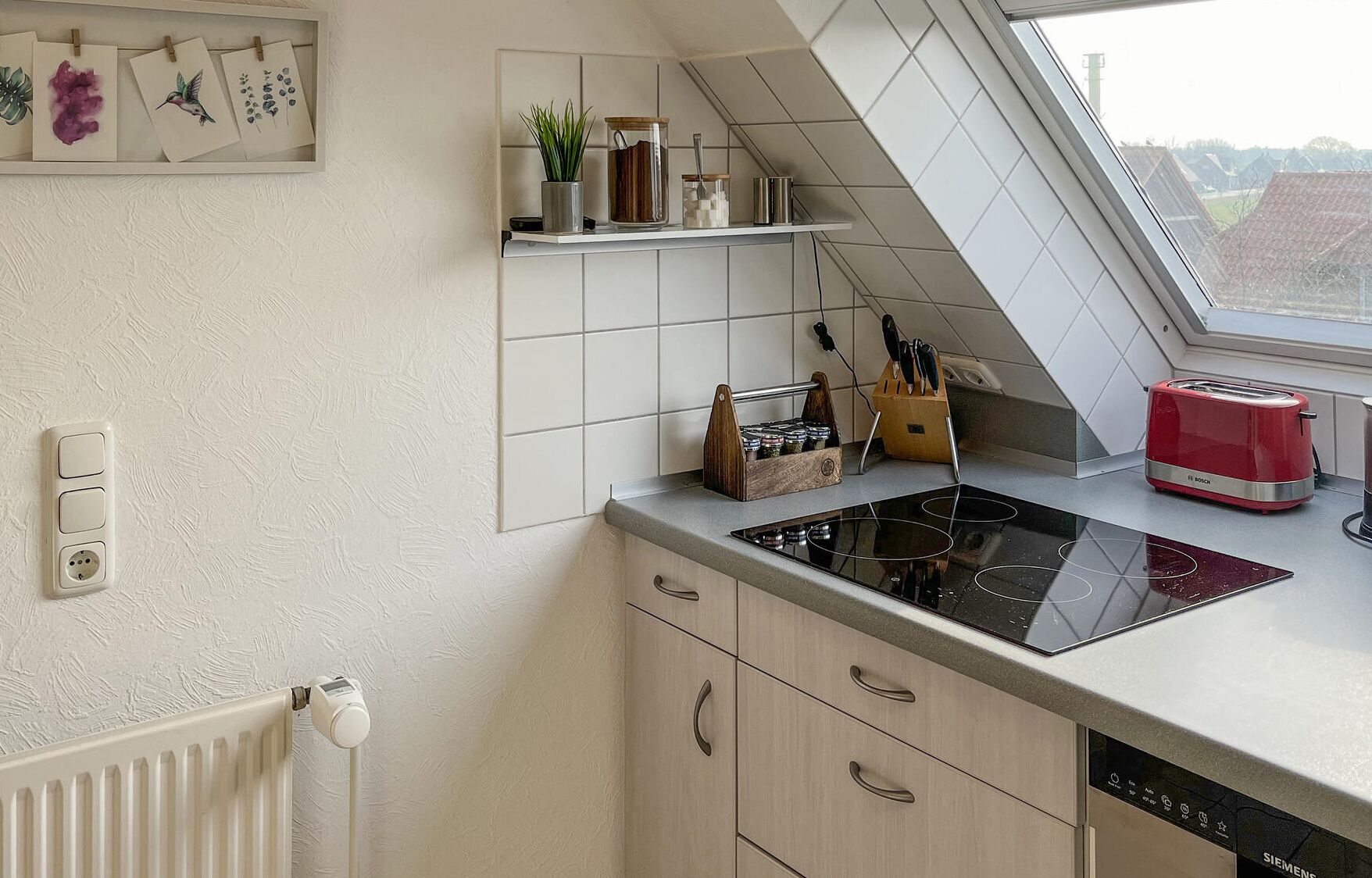 A modern kitchen with a built-in stove, a red toaster, and a window above the counter.