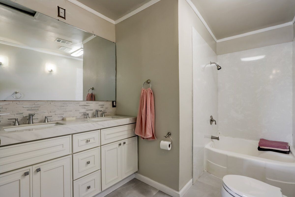A bathroom with a white sink, two mirrors, a bathtub, and a toilet.