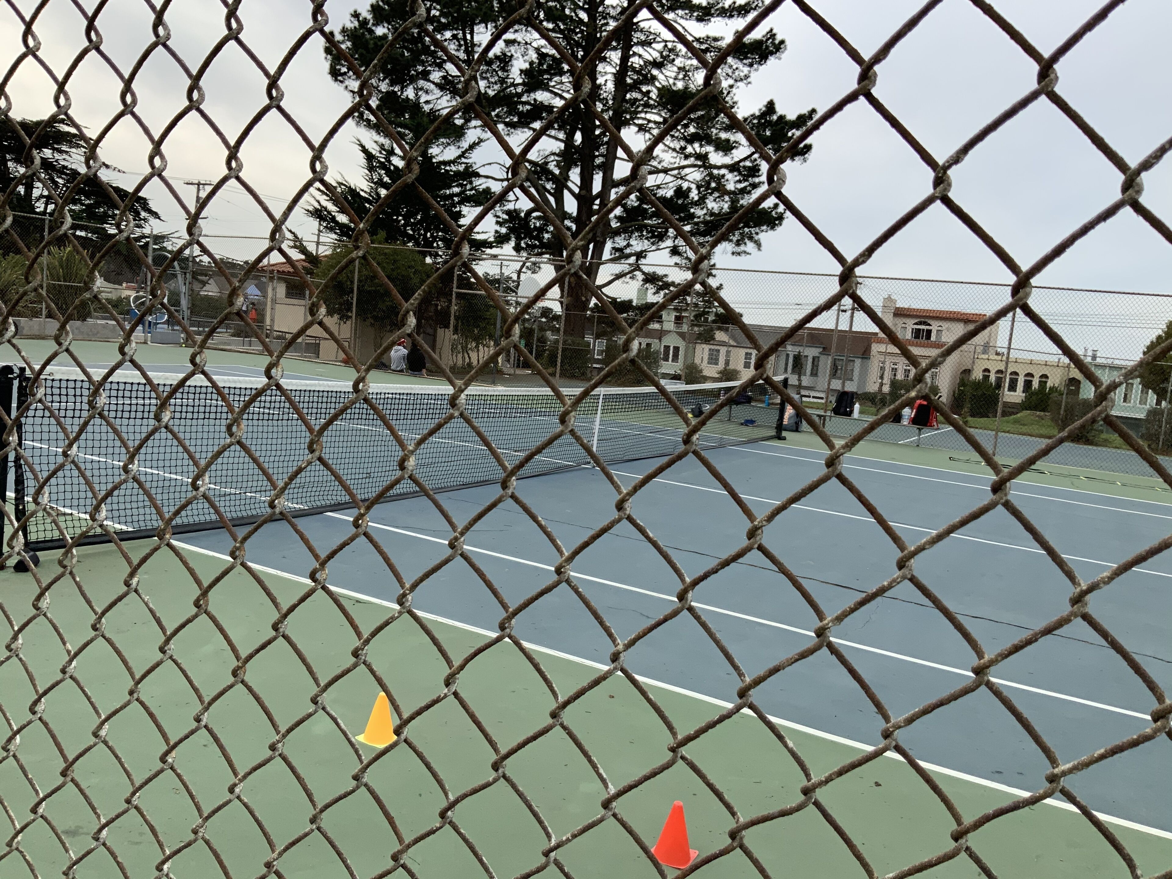 A chain-link fence surrounding a tennis court with a net.