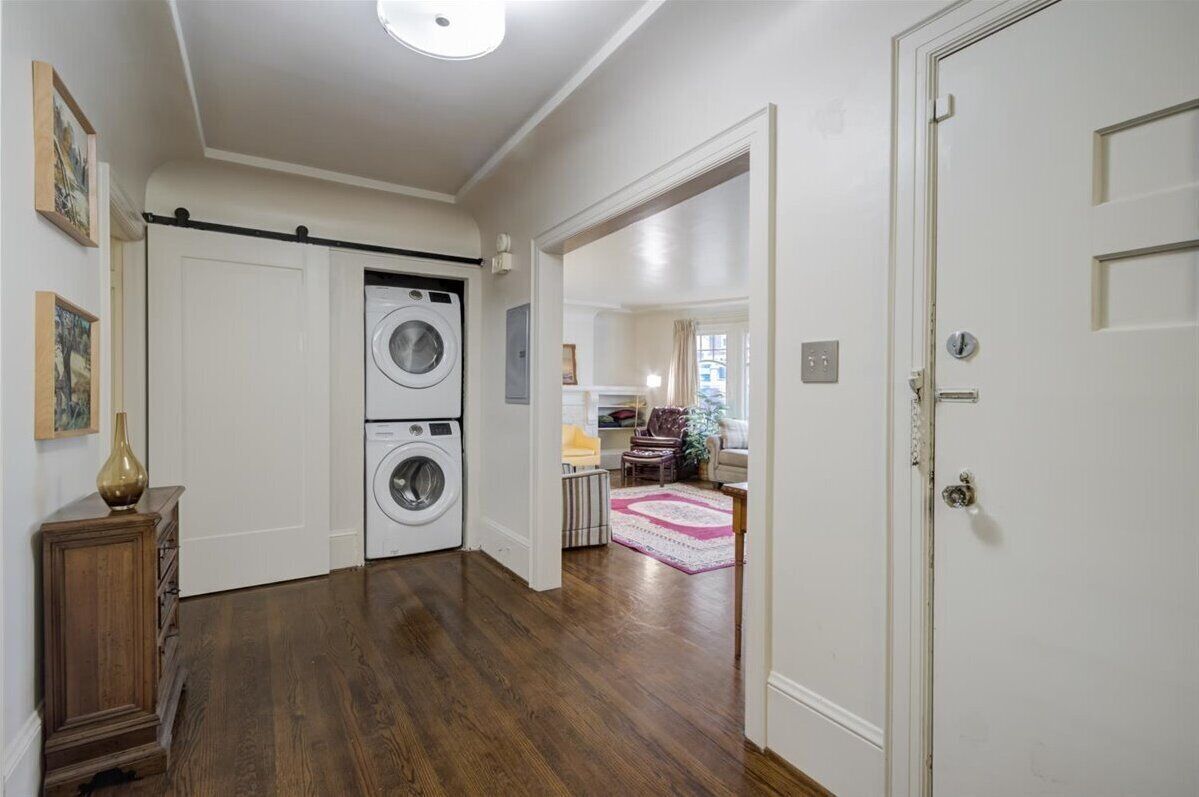 Una sala de bugaderia amb dues rentadores i una assecadora, un armari de fusta i una porta que dona a una altra estança.