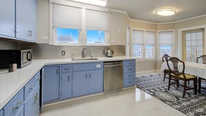 Eine moderne Küche mit blauen Schränken, einem Edelstahl-Geschirrspüler und einem Essbereich mit einem gemusterten Teppich.