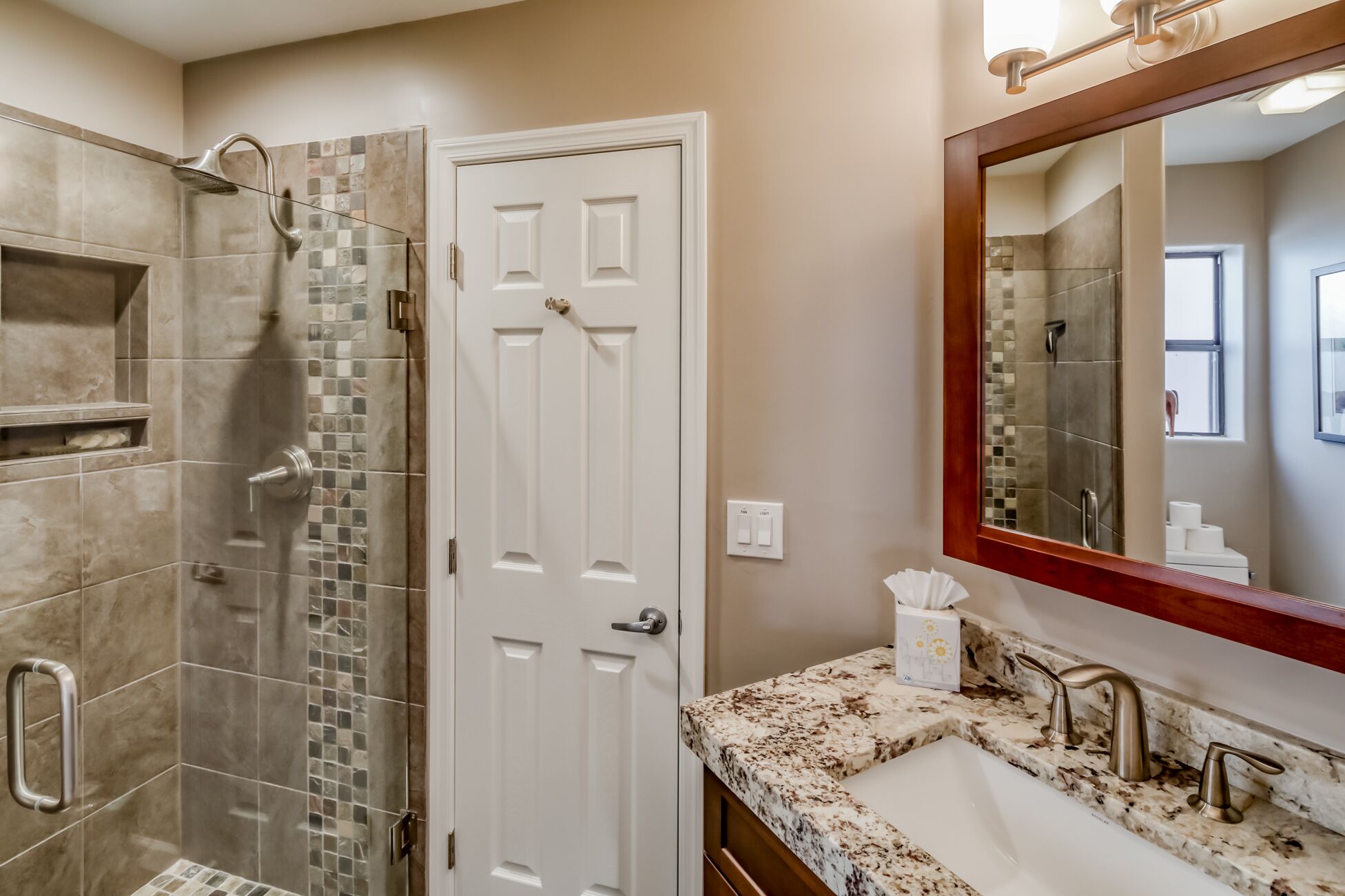 Une salle de bain avec une douche, un lavabo doté d’un plan de toilette en marbre et un miroir avec un cadre en bois.