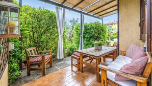 Un patio techado con una mesa y sillas de madera, un banco acolchado y vista a exuberante vegetación.