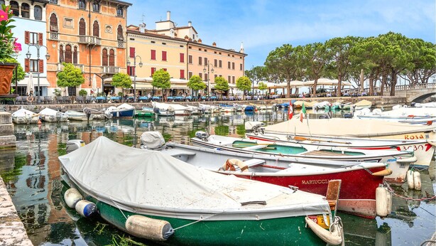 Una marina con barcos amarrados, un restaurante frente al mar y edificios históricos al fondo.