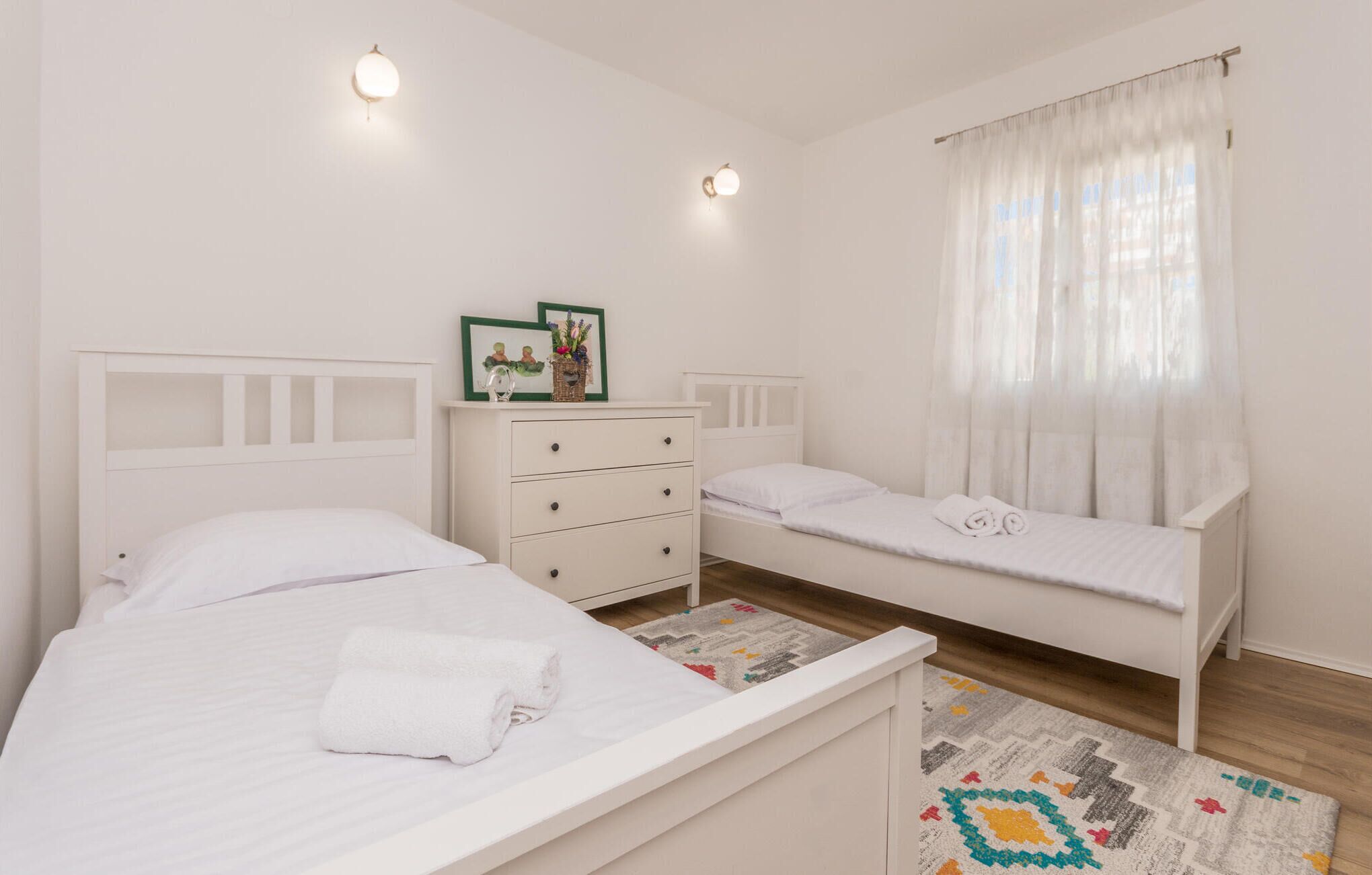 A bedroom with two single beds, a dresser, and a window with sheer curtains.