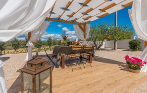 An outdoor dining area with a wooden table and chairs, white drapes, and a clear view of the surrounding landscape. - Amazing home in Polaca (Polaca)