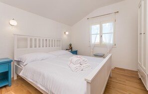 A bedroom with a white bed, a nightstand, a window with sheer curtains, and a wooden floor. - Amazing home in Polaca (Polaca)