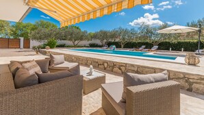 Zona de piscina al aire libre con mobiliario de mimbre y un toldo a rayas.