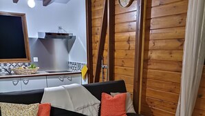Un salon avec un canapé noir, des coussins à motifs, un tapis à motifs géométriques et un mur en bois orné d’une horloge.