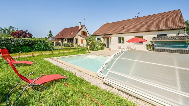 A swimming pool with a glass enclosure, red lounge chairs, and a house with a red-tiled roof. - Lovely home in Briare with sauna (Briare)