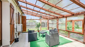A covered patio area with a green artificial turf, wicker furniture, and a view of the garden through large windows. - Lovely home in Briare with sauna (Briare)