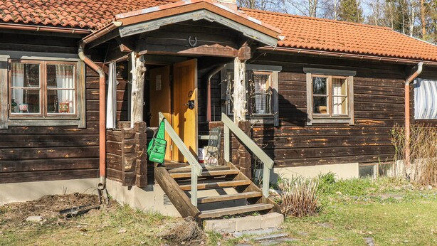 A wooden cabin with a red-tiled roof, a wooden staircase leading to the entrance, and a small porch area. - Amazing home in Enviken with lake view (Enviken)