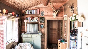 A cozy cabin interior with wooden walls, a television on a dresser, bookshelves, and various decorative items. - Amazing home in Enviken with lake view (Enviken)