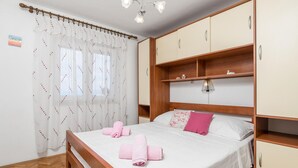 Ein Schlafzimmer mit einem hölzernen Bett, weißen Vorhängen, einer Nachttischlampe und einem kleinen Regal mit einem dekorativen Gegenstand.