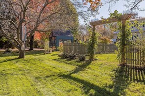 Ein gepflegter Garten mit einer Hollaube, einem eingezäunten Bereich und einem Haus im Hintergrund.