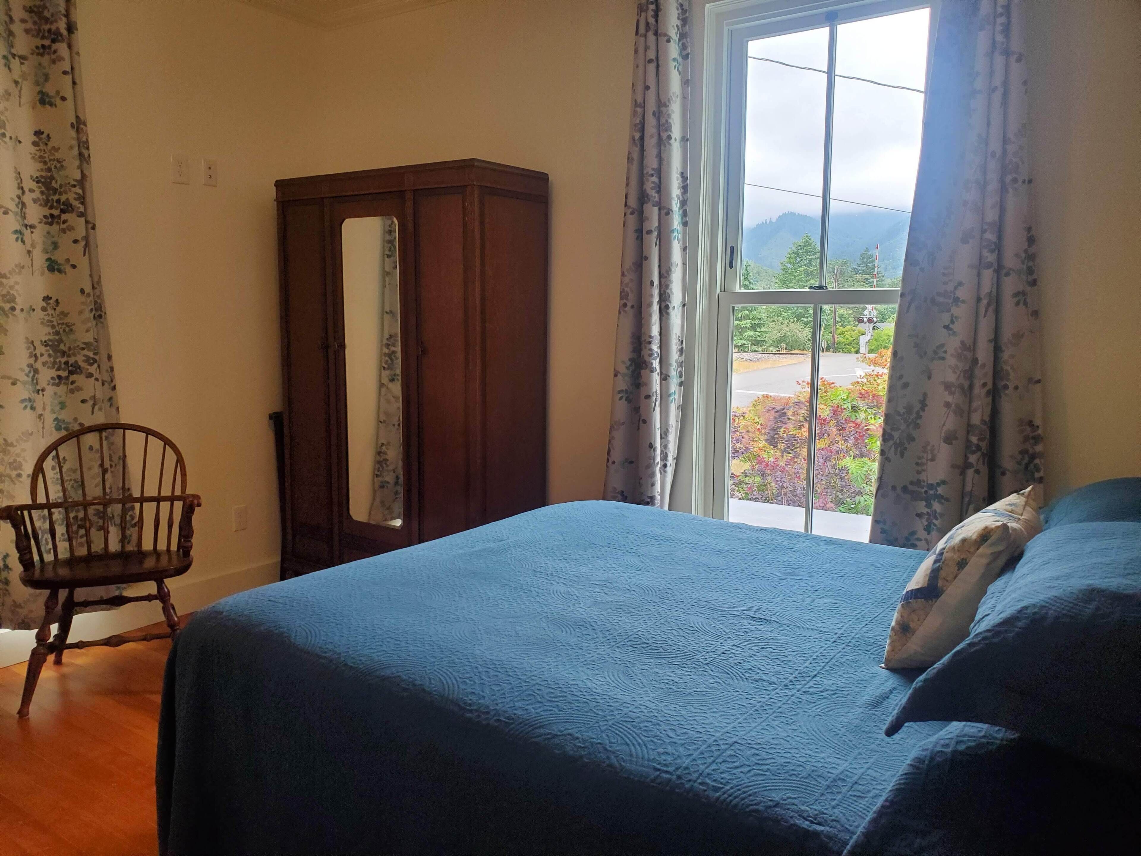 Un dormitorio con cama, una silla de madera, un armario y una ventana con vistas a zonas verdes.