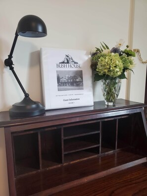A framed print of 'Bush House' with a black lamp and a vase of flowers on a wooden table.
