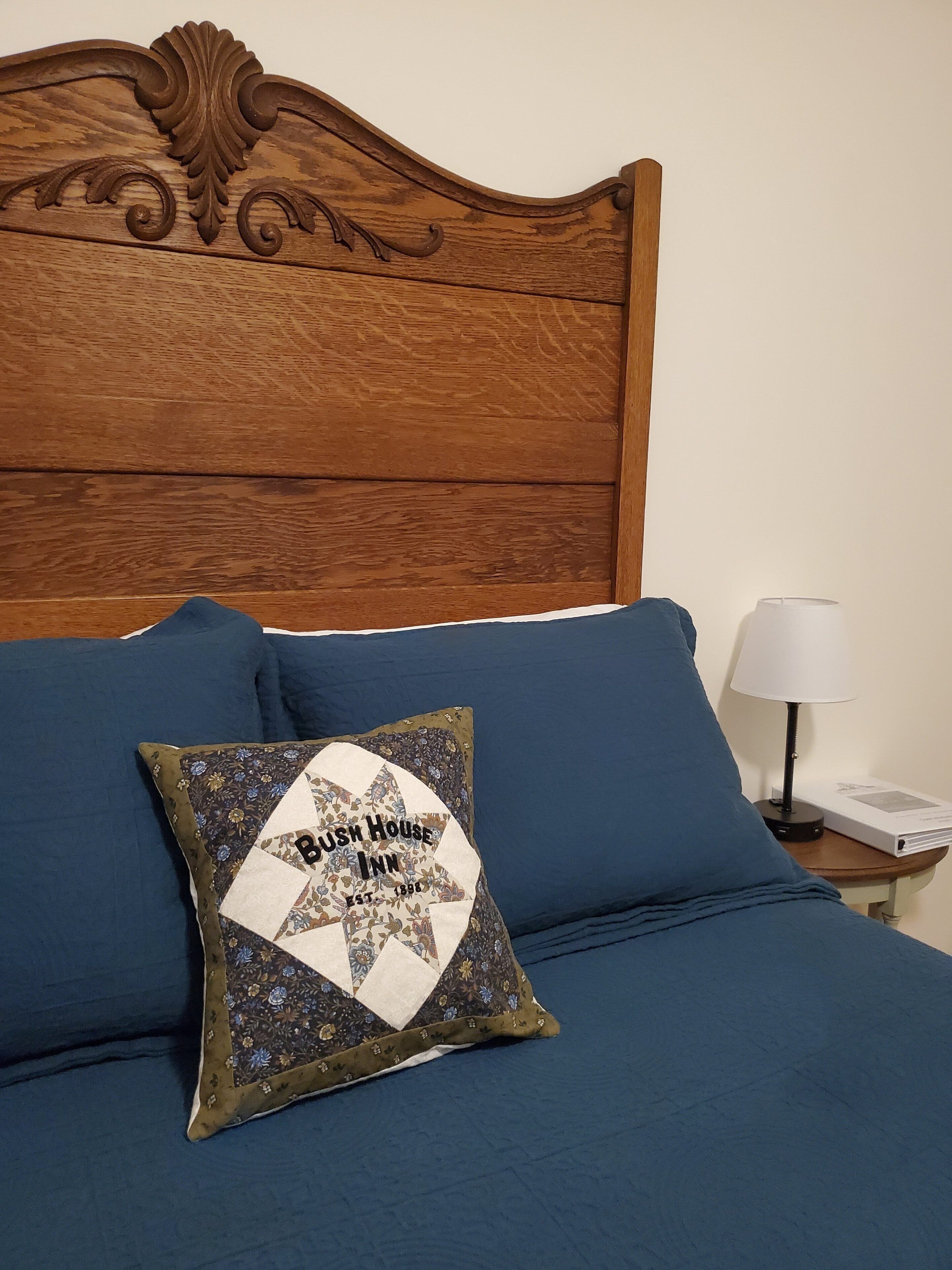 A bed with a quilted pillow, a wooden headboard, and a bedside table with a lamp and a book.