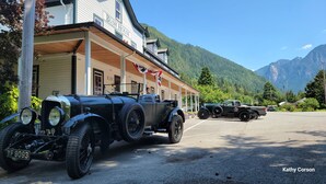 A vintage car parked in front of a building labeled "Bush House" with a mountainous backdrop. - Bush House Inn (Index)