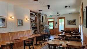 A restaurant with wooden tables and chairs, stone walls, and framed pictures on the walls. - Bush House Inn (Index)