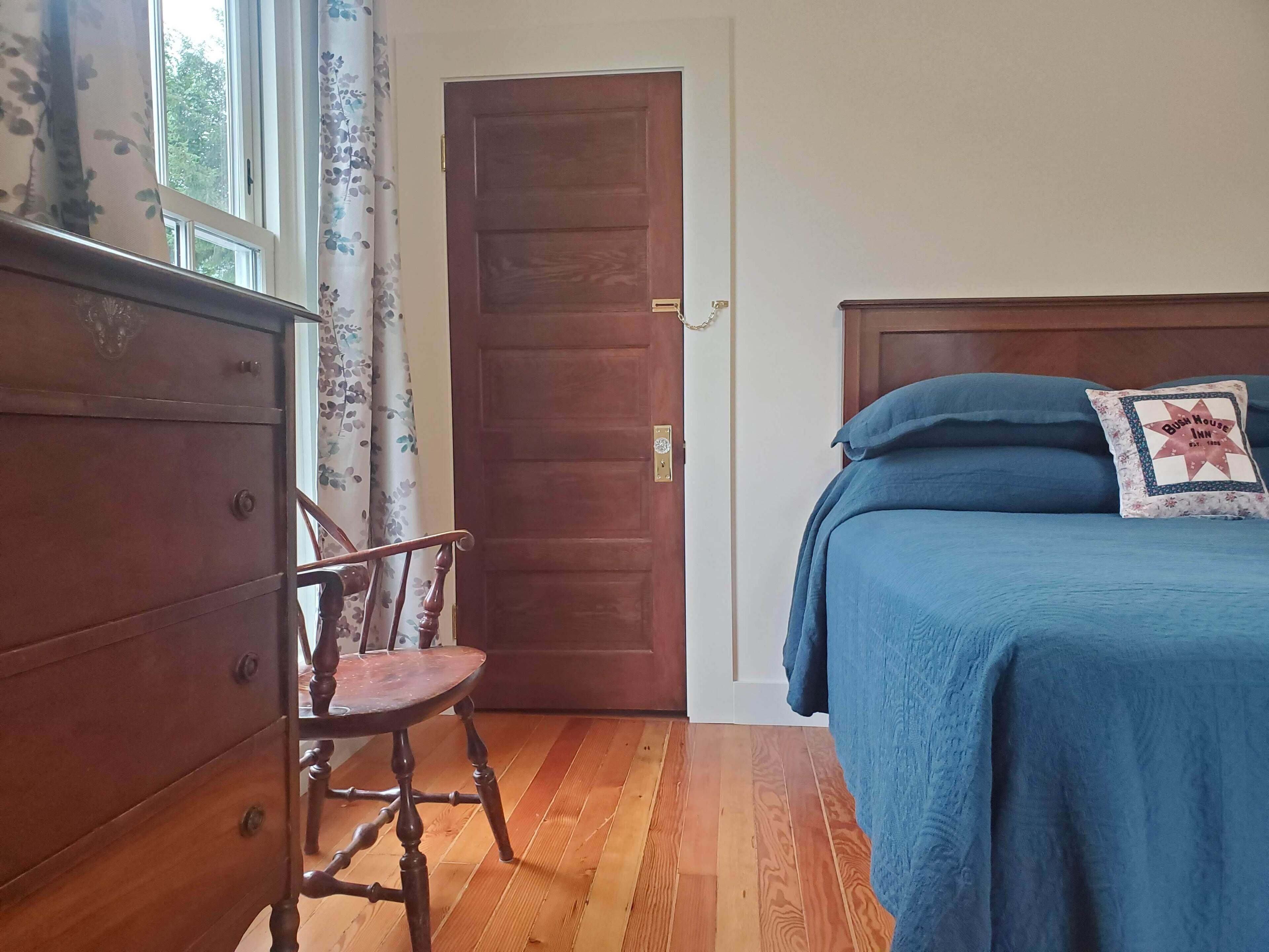Un dormitorio con un aparador de madera, una silla, una cama con ropa de cama azul y una puerta.