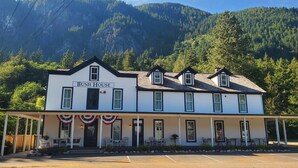 A two-story building named "Bush House" with a covered front porch, outdoor seating, and a view of a forested mountain range. - Bush House Inn (Index)
