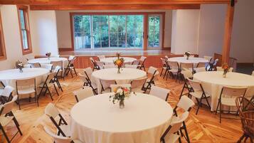 Un salón de conferencias con varias mesas redondas, sillas blancas y centros de mesa con flores.