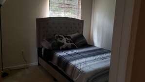 Un dormitorio con cama, mesita de noche y ventana con persianas.