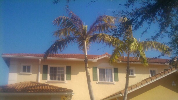 Una casa de dos pisos con techo de tejas rojas, contraventanas verdes y un garaje.