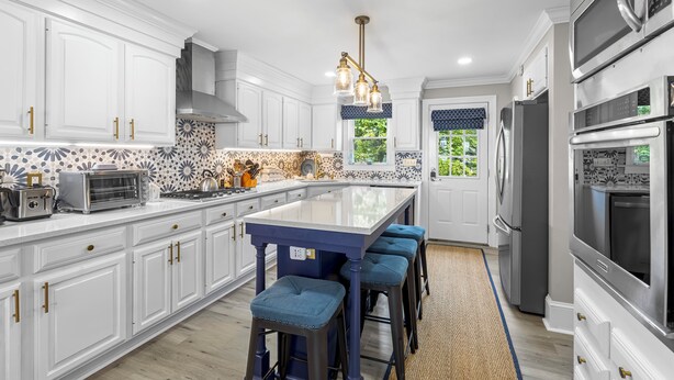 A modern kitchen with white cabinetry, a central island with stools, stainless steel appliances, and a decorative backsplash.