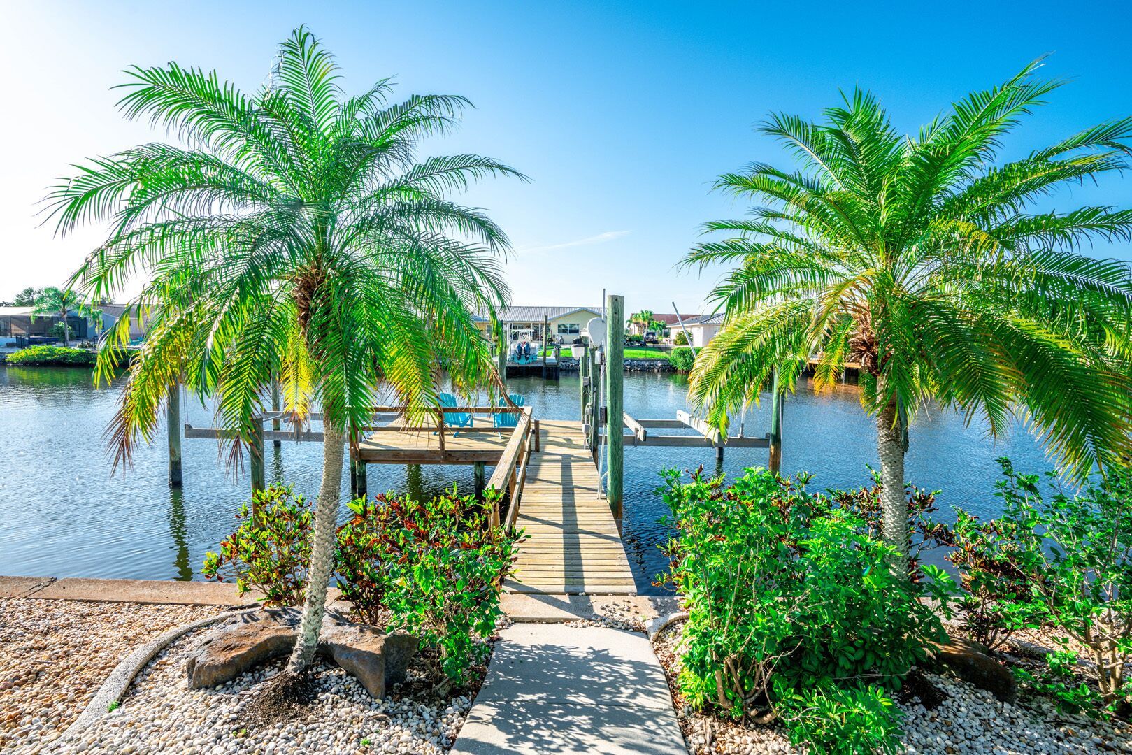 A wooden dock extending over calm water, surrounded by lush greenery and palm trees.