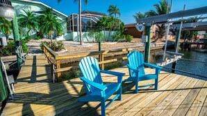 Una terraza de madera con dos sillas Adirondack azules, un área cubierta con cerramientos de vidrio y vistas a un cuerpo de agua.