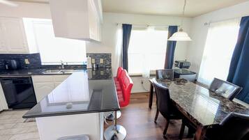 A modern kitchen with a central island, a dining area with a marble table, and a built-in oven.