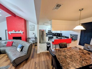 A modern living room with a red brick accent wall, a leather sofa, and a dining area with a marble table and red chairs. - Prime Location Arlington's Finest (Arlington)