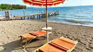 Ein Strand mit zwei Liegestühlen und einem gestreiften Strandsonnenschirm.