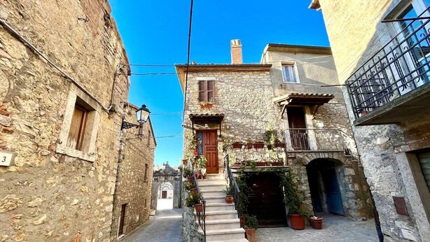 Eine enge Gasse aus Stein mit einer Treppe, die zu einem Gebäude mit einer Holztür und Blumentöpfen führt.