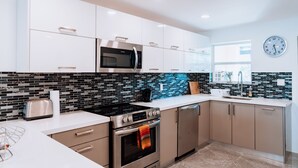Una cocina moderna con armarios blancos, un microondas negro, una estufa de acero inoxidable y un salpicadero de azulejos.