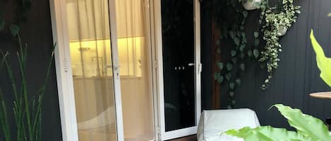 A wooden deck with a sliding glass door leading to a shower area, surrounded by potted plants and a white outdoor chair.