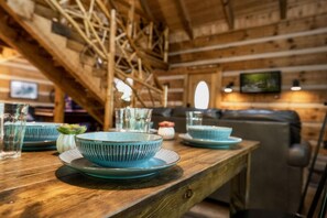 Een houten eettafel met blauwe keramieken borden en kommen, een glazen karaf en een kleine witte vaas met een groene plant.