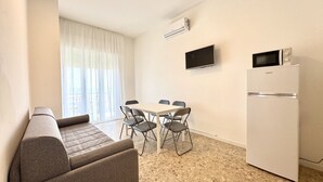 Ein gemütlicher Wohnbereich mit Sofa, Esstisch, Stühlen, Fernseher und Kühlschrank.