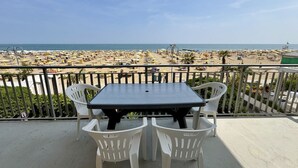 Ein Balkon mit Tisch und Stühlen mit Blick auf einen Strand mit Sonnenschirmen und Menschen.